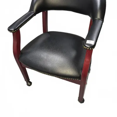 Sale Photo Thumbnail #12: Traditional black vinyl armchair featuring brass nailhead trim, a mahogany-finished wooden frame, and front caster wheels.