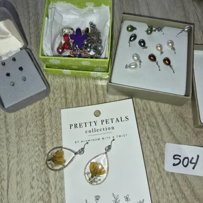 Sale Photo Thumbnail #867: Assortment of modern fashion jewelry, including pressed flower teardrop earrings by Pretty Petals, small stud earrings in a gray box, colorful pearl-style pendants, and an assortment of charms in a green box.