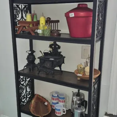 Sale Photo Thumbnail #574: Black metal etagere shelf displaying vintage kitchenware, ceramic goose napkin rings, miniature cast iron stoves, and small appliances.