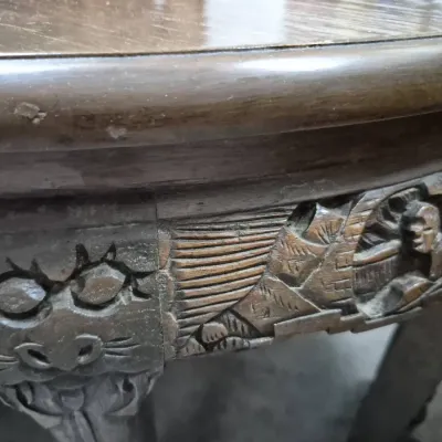 Sale Photo Thumbnail #166: Close-up of an intricately hand-carved Asian wooden table apron, featuring detailed figures and mask motifs with visible finish wear.
