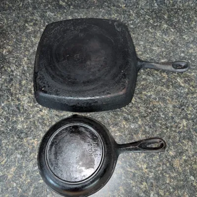Sale Photo Thumbnail #649: Two vintage cast iron cookware pieces including a square griddle pan and a No. 3 6 5/8-inch skillet, displayed upside down next to a ruler.