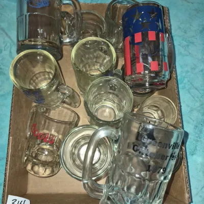 Sale Photo Thumbnail #549: Cardboard flat filled with assorted vintage beer mugs and shot glasses, including a 1979 Greenville Oktoberfest mug and a printed Coors glass mug.
