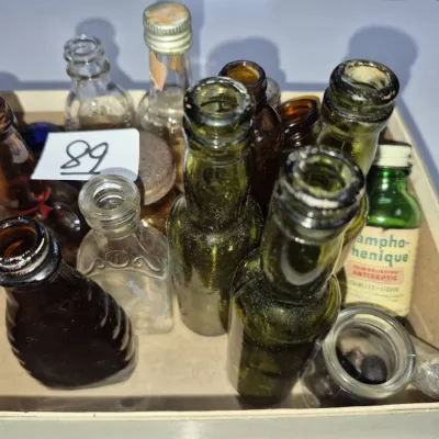 Sale Photo Thumbnail #143: Collection of vintage miniature glass medicine and apothecary bottles in amber, green, and clear glass, arranged inside a cardboard box.
