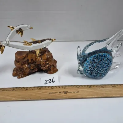 Sale Photo Thumbnail #389: Pair of glass aquatic animal figurines, including a glass dolphin sculpture with gold-tone accents on a burl wood base and a blue art glass fish figurine with patterned detailing.