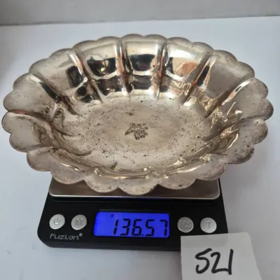 Sale Photo Thumbnail #899: Vintage scalloped silver bowl with engraved center motif, weighing 136.57 grams on a digital scale.