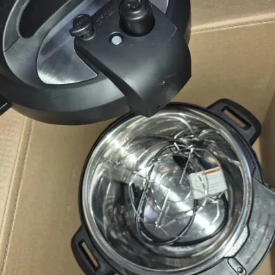 Sale Photo Thumbnail #551: Instant Pot electric pressure cooker with lid removed, showing the stainless steel inner pot, power cord, and wire trivet insert inside a cardboard box.