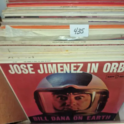 Sale Photo Thumbnail #756: Collection of vintage 33 RPM vinyl records stacked in a crate, featuring Bill Dana's comedy album "Jose Jimenez in Orbit" at the front.