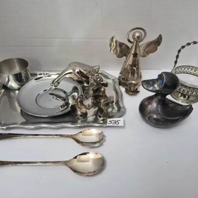 Sale Photo Thumbnail #923: Collection of silver-plated tabletop items, including serving spoons, small trays, duck and angel figurines, a basket dish, and a small metal cup, all displaying light tarnishing.