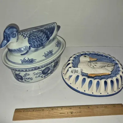 Sale Photo Thumbnail #748: Pair of blue and white ceramic duck-themed kitchen items, including a lidded casserole dish with a duck figure handle and a fluted oval tart pan or mold featuring a relief duck motif.