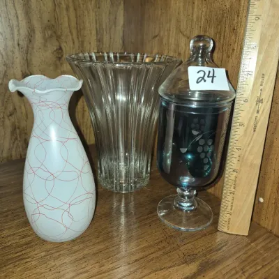 Sale Photo Thumbnail #38: Collection of decorative glassware including a white ruffled vase with red line pattern, a flared ribbed clear glass vase, and an etched lidded apothecary jar.