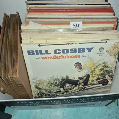 Sale Photo Thumbnail #755: Collection of vintage vinyl records stored in a cardboard box, featuring Bill Cosby's 1966 comedy album "Wonderfulness" at the front alongside a brown paper record album organizer.