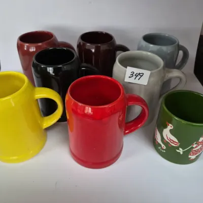 Sale Photo Thumbnail #608: Collection of seven vintage glazed ceramic mugs in various solid colors, including a green mug featuring a printed folk art motif.