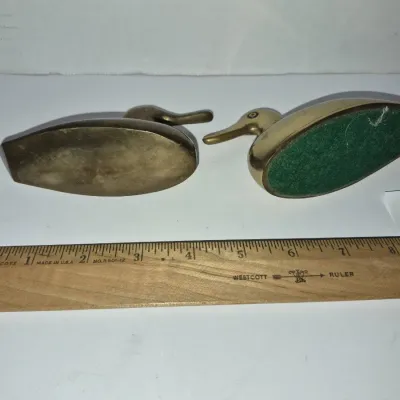Sale Photo Thumbnail #762: Pair of vintage solid brass duck paperweights or figurines, shown with a ruler for scale.