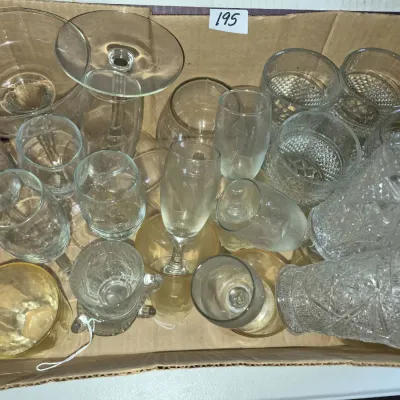 Sale Photo Thumbnail #334: Cardboard box filled with assorted vintage glassware, including wine stems, champagne flutes, press-cut tumblers, and small bowls.