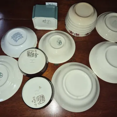 Sale Photo Thumbnail #46: Collection of vintage ceramics displayed upside down on a wooden surface, including saucers, small bowls, cups, and a square vessel featuring various maker's marks.