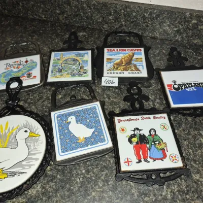Sale Photo Thumbnail #718: Collection of vintage cast iron framed decorative ceramic tile trivets, featuring souvenir, animal, and regional folk art designs.