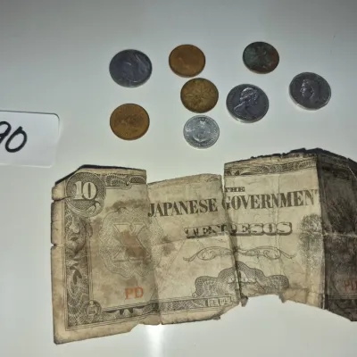 Sale Photo Thumbnail #144: A heavily worn World War II Japanese government-issued 10 Pesos occupation banknote alongside a small assortment of international coins.
