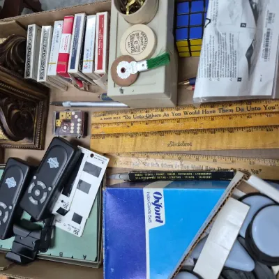 Sale Photo Thumbnail #172: Cardboard box filled with assorted vintage office supplies, playing cards, wooden rulers, small electronics, and decorative items.