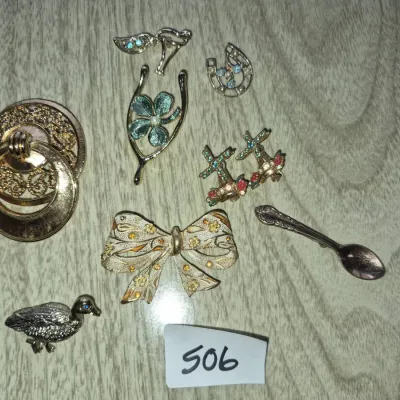 Sale Photo Thumbnail #870: Collection of vintage costume jewelry brooches and pins, including novelty designs such as a duck, a spoon, a floral bow, a horseshoe, and windmills.