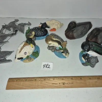 Sale Photo Thumbnail #827: Collection of duck-themed decor, including painted resin figurines, wooden decoys, and pewter ornaments.
