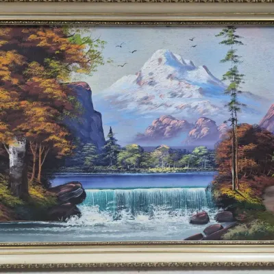 Sale Photo Thumbnail #495: Framed oil painting of a mountain landscape featuring a waterfall, autumn trees, and snow-capped peaks in an ornate cream-and-gold frame.