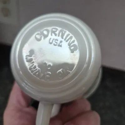 Sale Photo Thumbnail #668: Bottom detail of a vintage white Corning milk glass mug, featuring raised maker's marks including "Corning" and "Microwave OK."