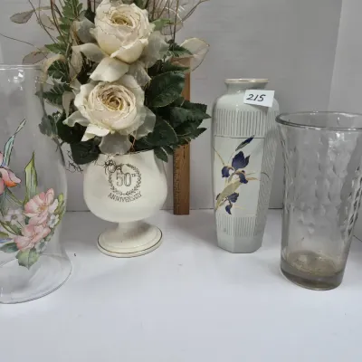 Sale Photo Thumbnail #368: Collection of decorative vases, including a glass hurricane shade with painted floral designs, a 50th-anniversary pedestal vase with faux white roses, an iris-patterned ceramic vase, and a textured clear glass vase.