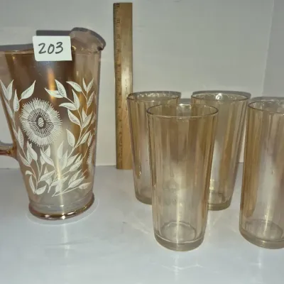 Sale Photo Thumbnail #345: Vintage marigold iridescent carnival glass water pitcher set with a white floral pattern, accompanied by four matching ribbed tumblers.