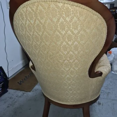 Sale Photo Thumbnail #110: Vintage Victorian-style upholstered armchair featuring a carved wooden crest, gold damask fabric, and braided gimp trim, seen from the rear.