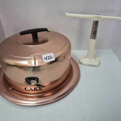 Sale Photo Thumbnail #813: Vintage copper-colored metal cake carrier with lid and tray alongside an off-white paper towel holder.