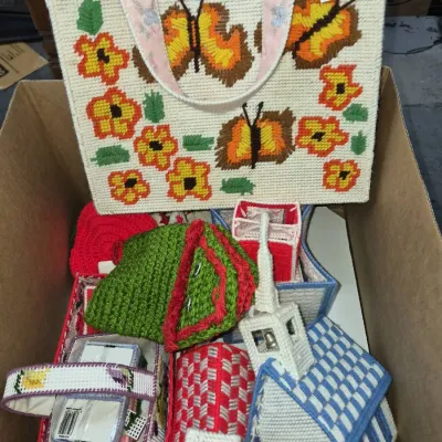 Sale Photo Thumbnail #146: Box filled with vintage handcrafted plastic canvas needlepoint crafts, including a tote bag featuring butterflies and flowers alongside decorative tissue box covers.