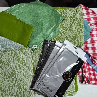Sale Photo Thumbnail #197: Collection of assorted linens, including green lace tablecloths, red and white gingham fabric, and packaged Grandpity plastic table covers.
