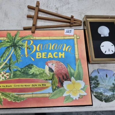 Sale Photo Thumbnail #206: Collection of tropical-themed decor items including a large 'Banana Beach' print, framed seashell shadowbox, small wooden easel, and a hand-painted sand dollar.