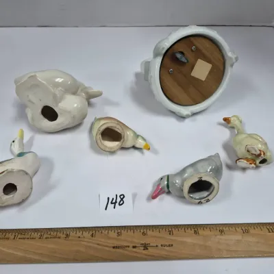 Sale Photo Thumbnail #253: Collection of five vintage ceramic duck figurines alongside a ceramic music box, shown upside down revealing base openings and winding mechanism.