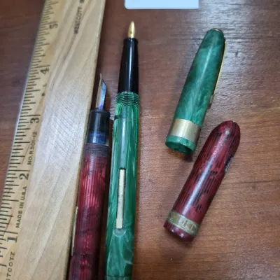 Sale Photo Thumbnail #181: Two vintage marbled fountain pens, one green and one red, shown disassembled next to a ruler.