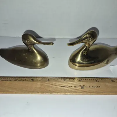 Sale Photo Thumbnail #761: Pair of vintage solid brass duck figurines, measuring approximately four inches long each, shown with a Westcott wooden ruler for scale.