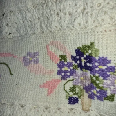 Sale Photo Thumbnail #84: Handmade white crocheted textile with embroidered floral motifs in shades of purple, green, and pink, trimmed with decorative lace edging.