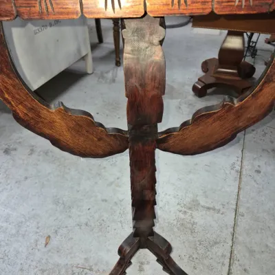 Sale Photo Thumbnail #126: Hand-carved wooden pedestal tilt-top side table featuring an ornate central column and tripod base. The table shows a dark stained finish with minor surface wear.