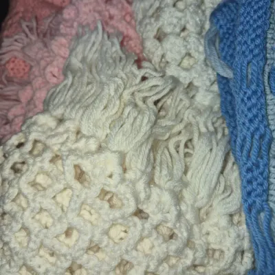 Sale Photo Thumbnail #73: Collection of handmade crochet and knit afghans with fringe details in cream, pink, and blue yarn.