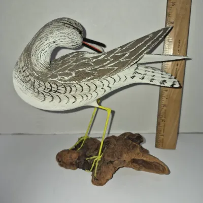 Sale Photo Thumbnail #273: Hand-carved and painted wooden shorebird decoy, depicted preening and mounted on a driftwood base, measuring approximately 8 inches tall.
