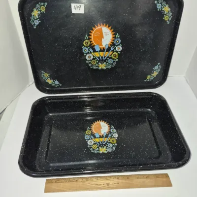 Sale Photo Thumbnail #734: Vintage black speckled enamelware roasting pan with lid, featuring a sun motif and floral accents, accompanied by a 12-inch wooden ruler for scale.