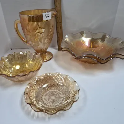 Sale Photo Thumbnail #304: Four-piece collection of marigold carnival glassware including a footed pitcher with floral motif and three ruffled bowls with varied geometric patterns.