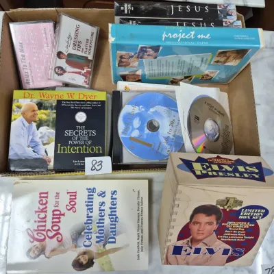 Sale Photo Thumbnail #133: Box lot of media including audio cassettes, CDs, VHS tapes, a 'Chicken Soup for the Soul' book, and a wooden Elvis Presley limited edition CD box set.