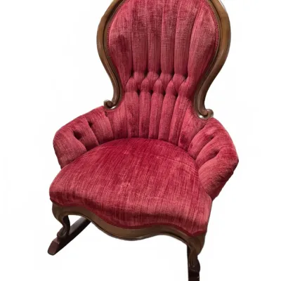 Sale Photo Thumbnail #104: Victorian-style tufted platform rocking chair upholstered in red velvet with a carved wooden frame featuring floral details on the crest.