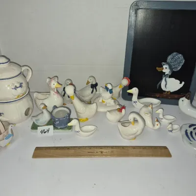 Sale Photo Thumbnail #800: Collection of country-style white goose and duck ceramics, including figurines, small planters, a teapot warmer, and a framed chalkboard.