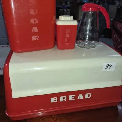 Sale Photo Thumbnail #58: Vintage mid-century red and white plastic kitchen set, including a roll-top bread box, sugar canister, salt shaker, and glass syrup dispenser.