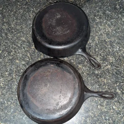 Sale Photo Thumbnail #655: Pair of vintage cast iron skillets, including an 11 3/4-inch Wagner Ware or unmarked Wagner skillet with noticeable surface wear and patina.