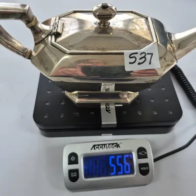 Sale Photo Thumbnail #926: Vintage silver-plated rectangular teapot with geometric Art Deco lines and an angular handle, shown on a digital scale weighing 556 grams.