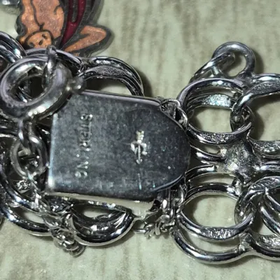Sale Photo Thumbnail #864: Close-up of a sterling silver charm bracelet box clasp with a maker's mark and an enamel charm attached.