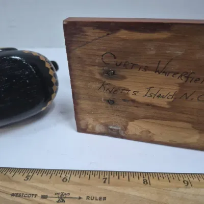 Sale Photo Thumbnail #454: Hand-carved wooden duck decoy base showing the maker's signature, "Curtis Waterfield, Knotts Island, N.C.", alongside a small painted decoy.